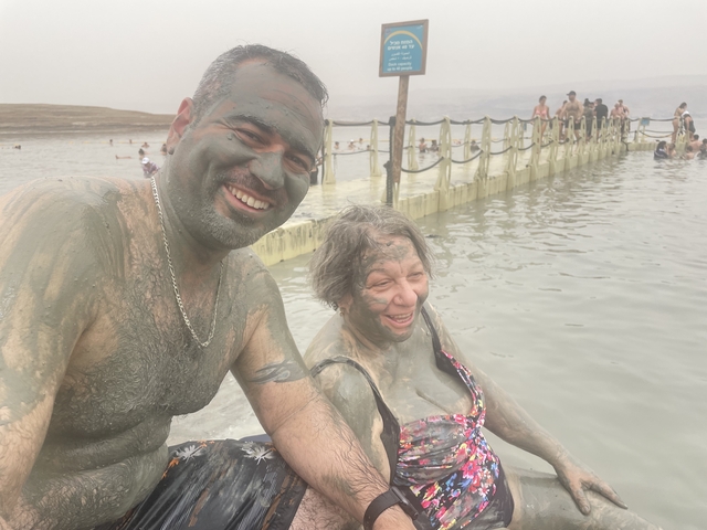       Two people covered in mud at a popular spa.
  