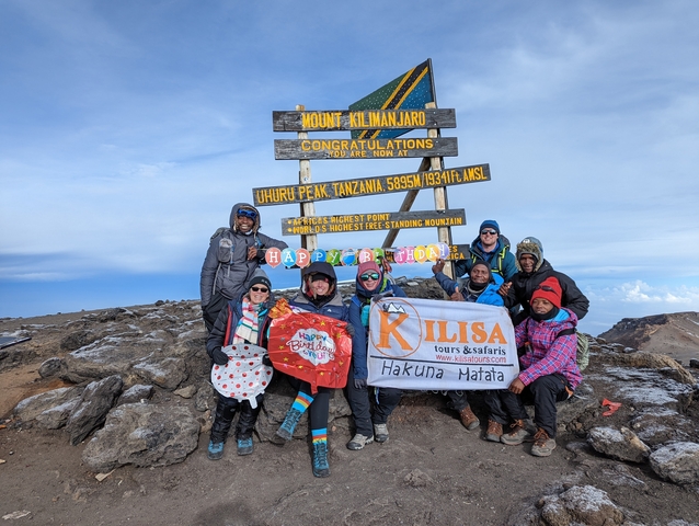       Group of people at the summit of Mount Kilimanjaro with a congratulatory sign.
  