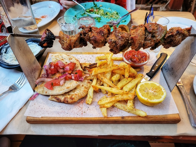 Plate of skewered meat, pita bread, fries, and sauce.