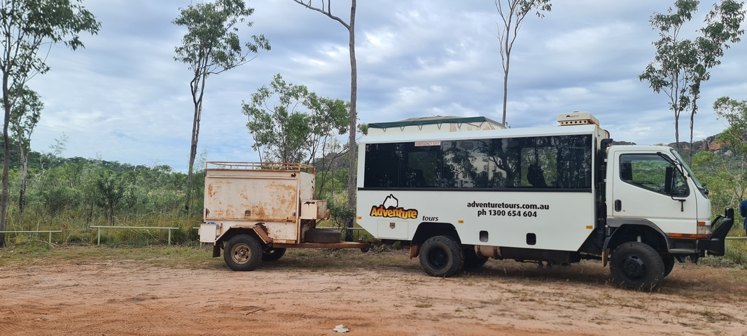       A tour bus parked on a dirt road amidst greenery.
  