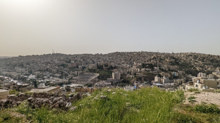 Hilly cityscape with a dense cluster of buildings under a bright sky.