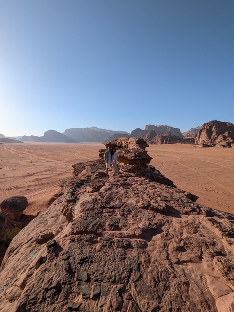      Two people standing on a rocky outcrop with a desert landscape behind.
  