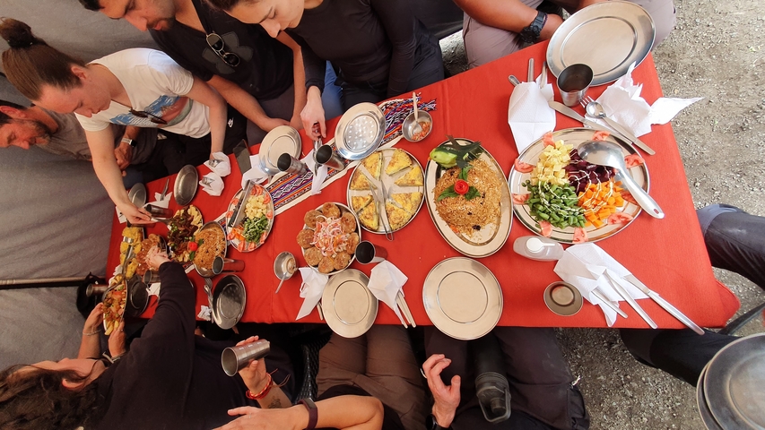 Group of people dining with diverse dishes on a red tablecloth.