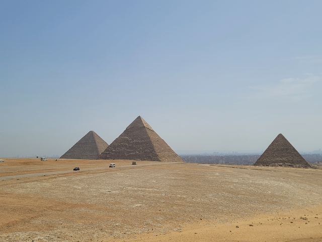 Panoramic view of the pyramids in Giza desert under a blue sky.