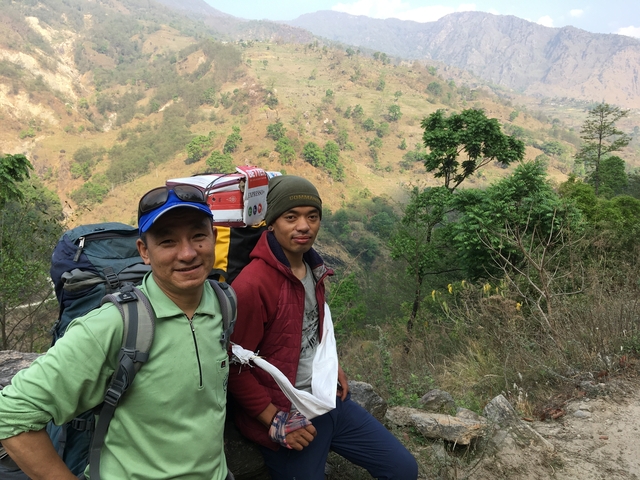 Two male trekkers standing with backpacks in a hilly area.