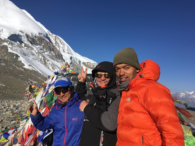 Three people posing with snowy mountains and prayer flags.