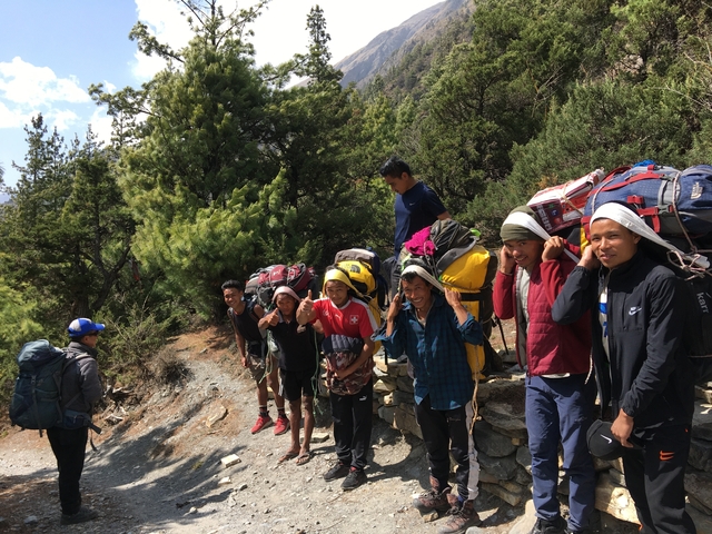 Group of trekkers carrying heavy bags in a forested area.