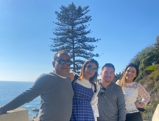 A group of people posing in front of a large tree and ocean view.