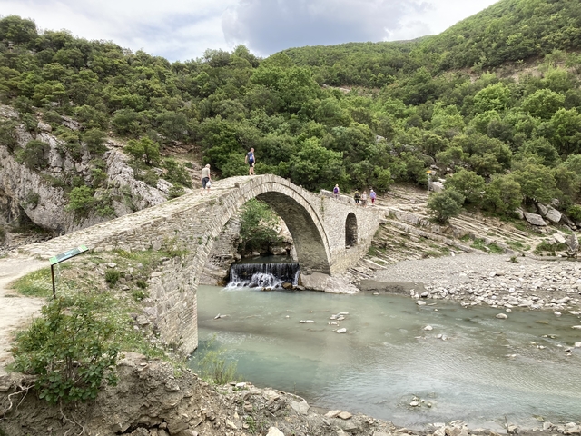       Stone bridge crossing a river with people walking on it.
  