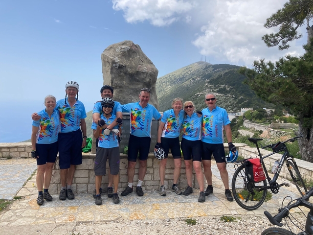       Group of cyclists posing with a mountain in the background.
  