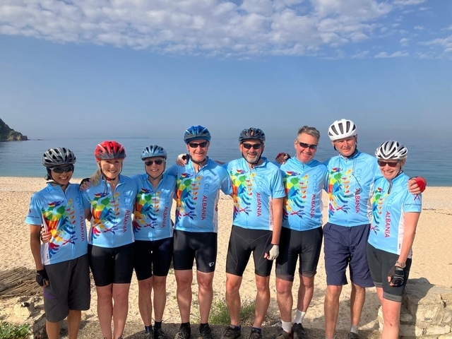       Group of cyclists wearing matching jerseys on a beach.
  