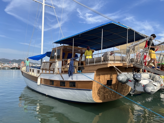 People on a wooden boat docked at a marina on a sunny day.