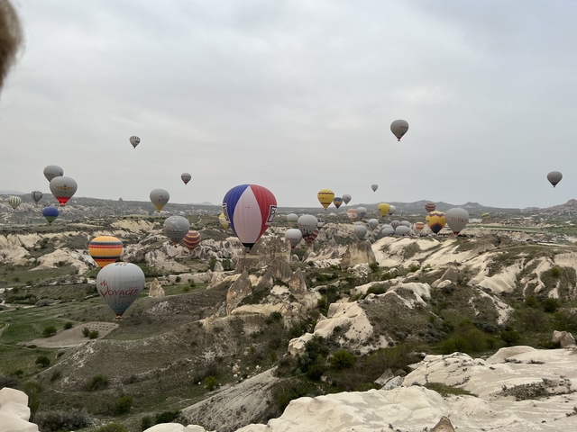 Many hot air balloons in the sky over Cappadocia's rock formations.