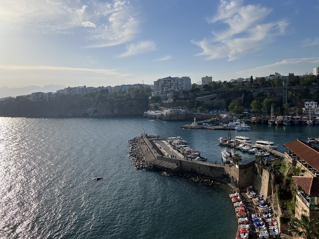 View of a harbor with boats and city buildings, surrounded by sea.