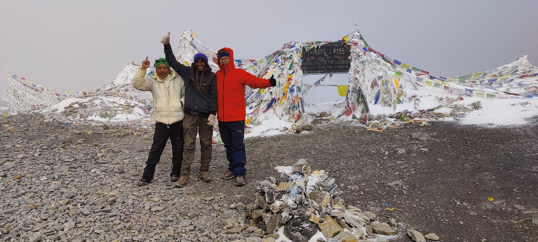 Group celebrating at Thorong La Pass; prayer flags visible.