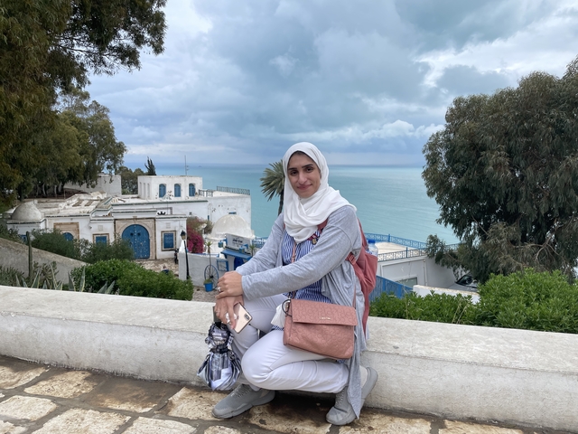       A person sitting on a ledge with a scenic view of the sea and buildings below.
  