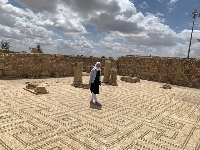       Person standing on an ancient tiled floor with ruins around.
  