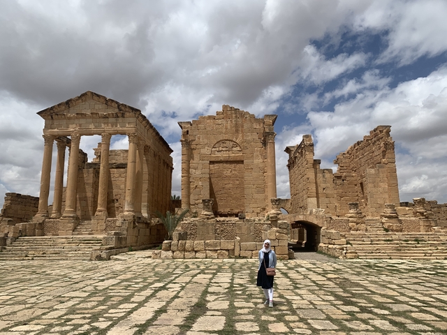       Person standing in front of ancient ruins with cloudy skies.
  