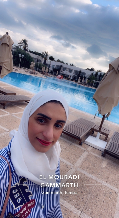       Selfie by a pool with poolside loungers.
  