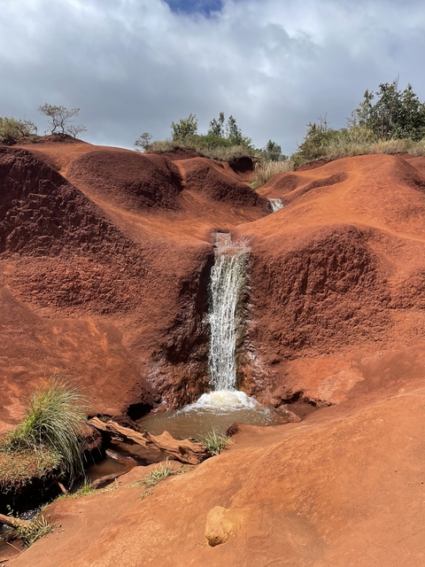 Small waterfall flowing through red soil formations.
