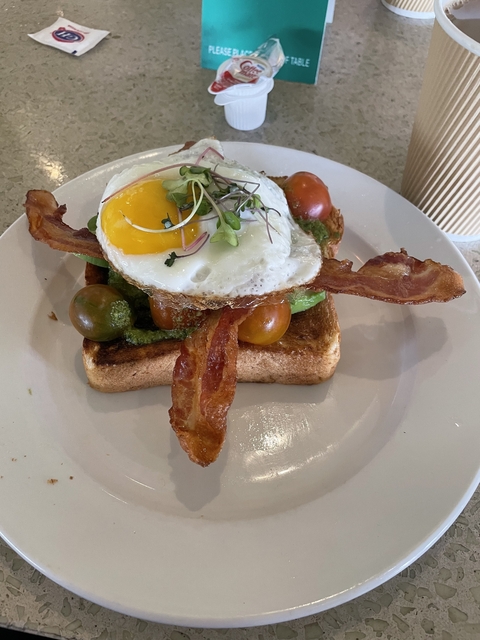 Plated breakfast with toast, bacon, egg, and tomatoes.
