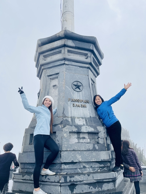 Two women smiling near the Fansipan summit marker.