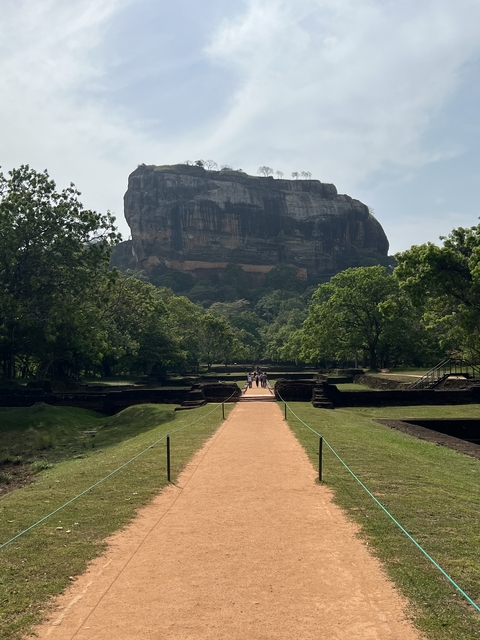 Sigiriya Rock in the background with people walking on a path.