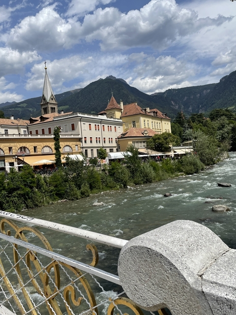 River flowing alongside historic buildings with mountain backdrop.