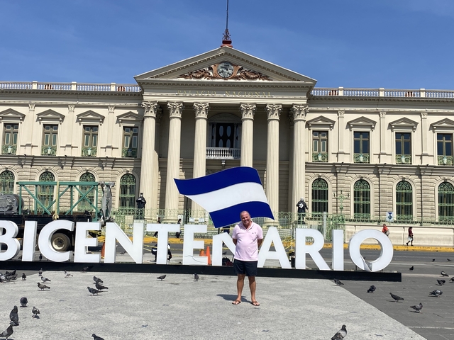       Man standing in front of a grand building holding a flag.
  