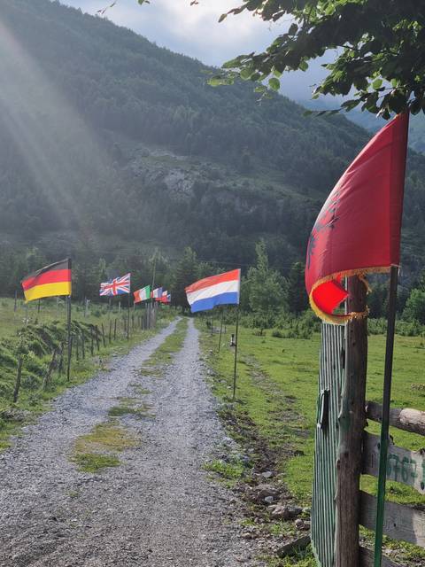Flags on poles along a pathway with mountains in the background.