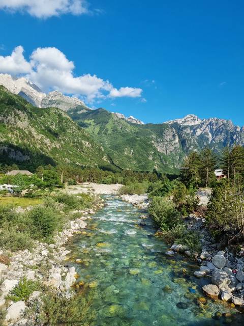       Clear river running along a rocky terrain with mountains.
  
