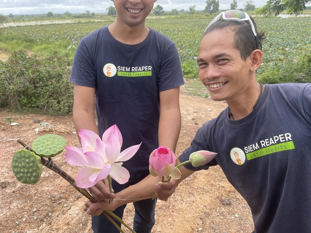 Two people holding lotus flowers, smiling at the camera.