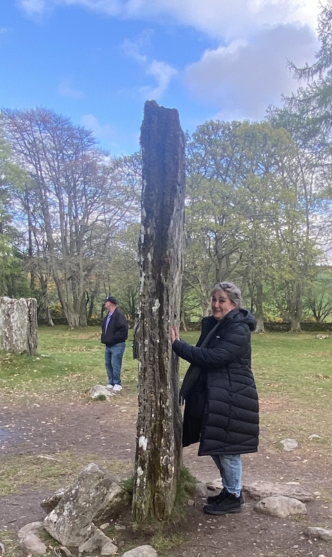      Person hugging a large standing stone in a field.
  