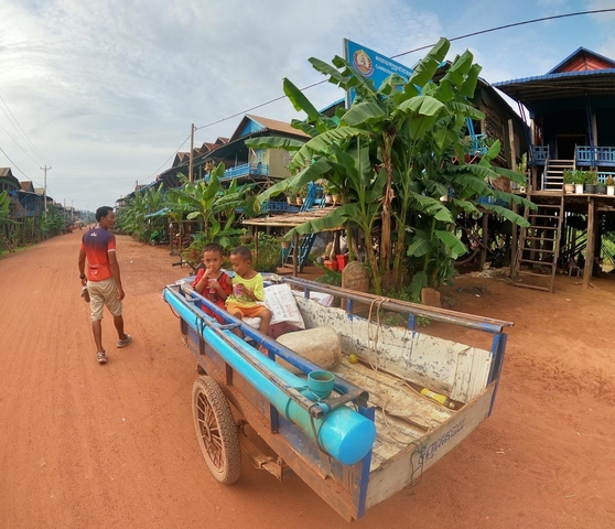       Children in a cart passing stilt houses.
  
