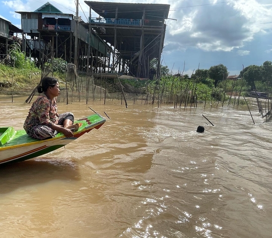       Woman in a boat in river, village in background.
  