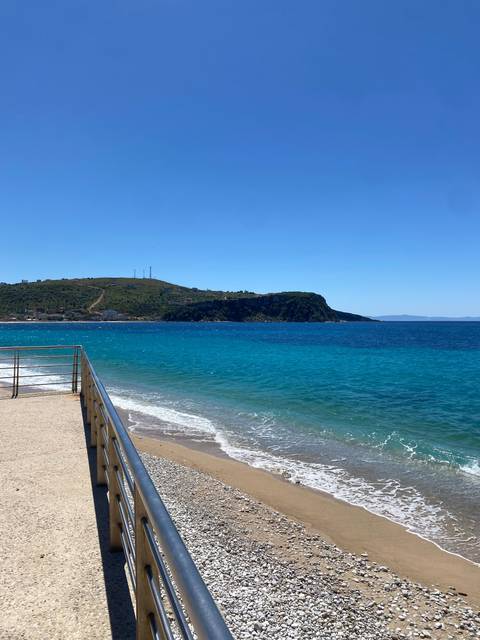       A beach with clear blue water and hills.
  