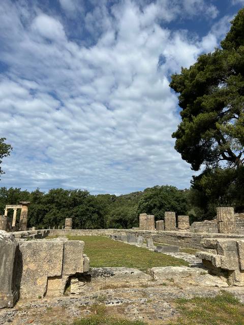 Ancient site with stone columns and trees under a blue sky.