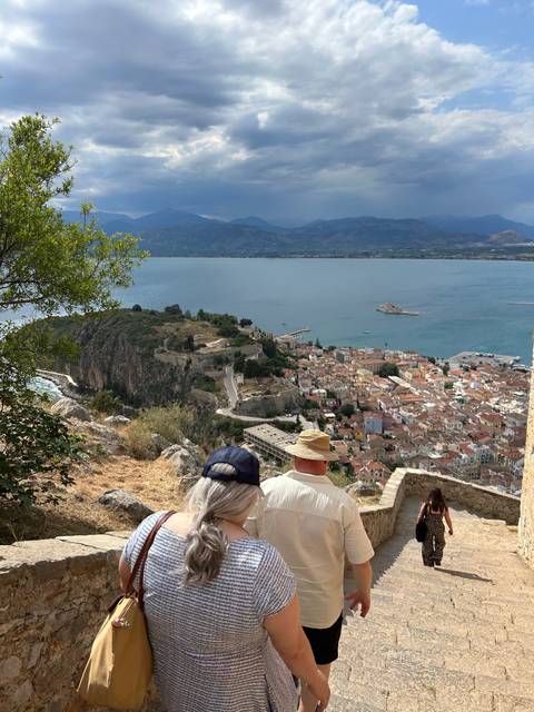       People walking down a stone path with a seascape in the background.
  