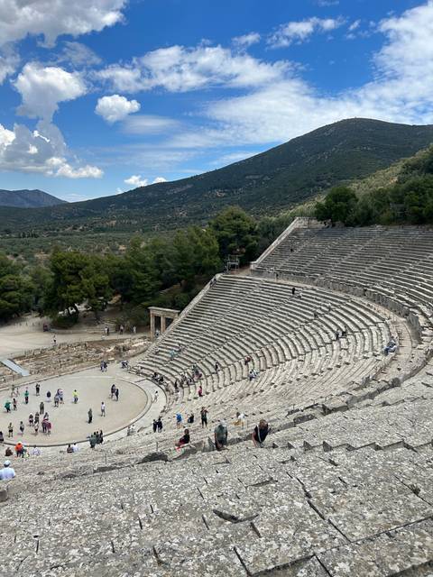       A large amphitheater with seated visitors and a mountainous backdrop.
  
