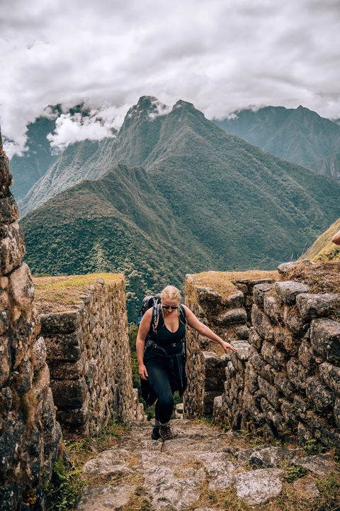 Woman climbing ancient stone steps with green mountains.