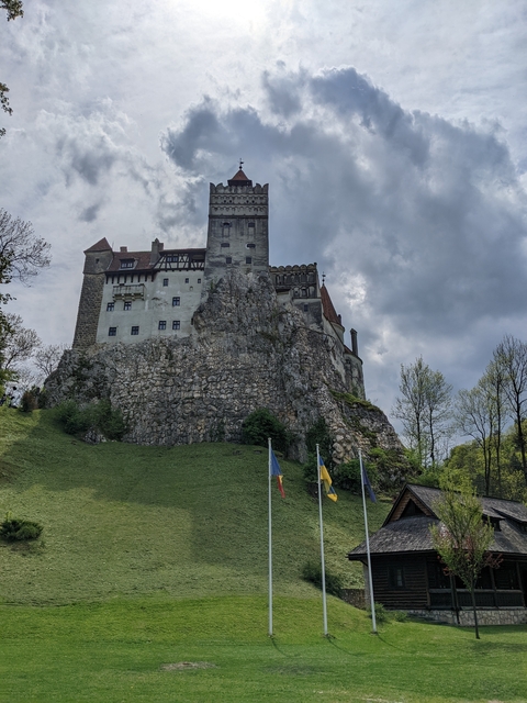 Bran Castle perched on a rocky hill with flags in front.