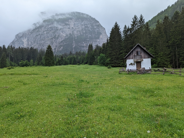 Lonely cottage with an overcast sky and tall trees, against a mountainous backdrop