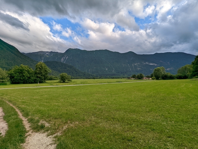       Vast green field with mountains in the background under a partly cloudy sky
  