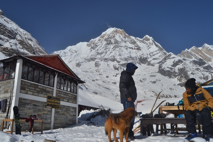      Two people sitting outside a mountain lodge with snow-covered peaks
  
