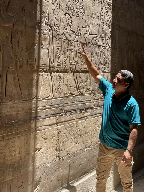 Person pointing at hieroglyphics on an ancient wall.