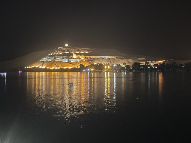 Night view of a lit hill reflecting in a river.