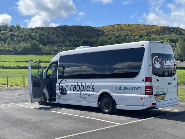 Tour bus parked in a rural area with hills in the background.