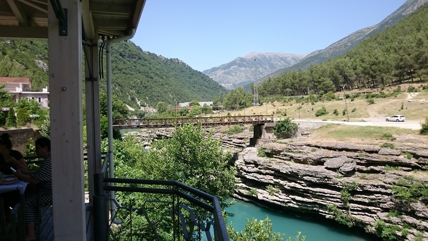       A scenic view of a wooden bridge over turquoise water in a mountainous area.
  