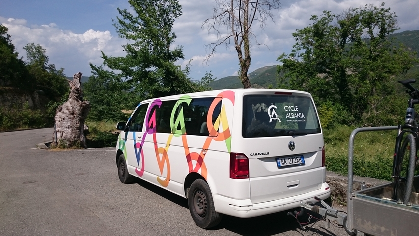       A parked van with 'Cycle Albania' branding, set in a rural area.
  