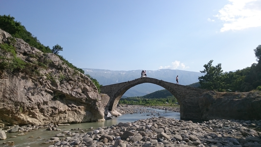       An arched stone bridge with people walking over it, set in a rocky landscape.
  